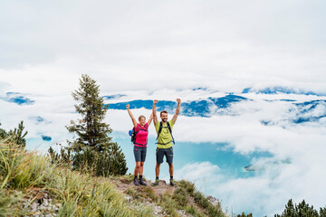 Happy young couple with raised arms on a hiking trip in the mountains, Herzogstand, Bavaria, Germany