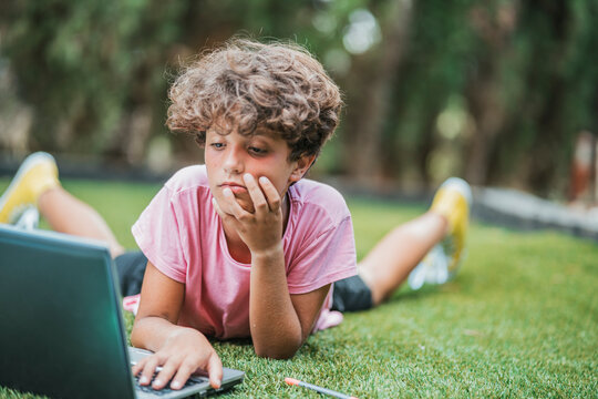 Boy lying in grass using laptop