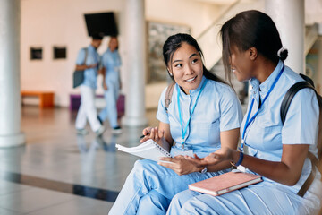 Asian nursing student and her female friend talk while studying in hallway at medical university. - obrazy, fototapety, plakaty