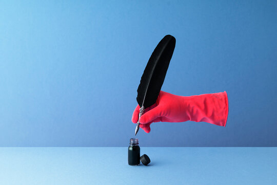 Quill pen held in hand and dipping in inkwell over blue background