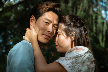 Obraz premium Attractive korean young man looking at camera while beautiful woman with long hair is hugging him under sunset at the park