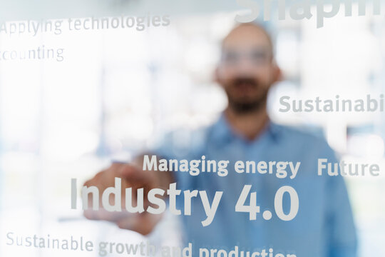 Businessman in front of glass pane pointing on words, industry 4.0