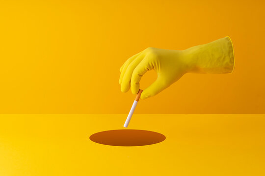 Hand dicarding cigarette into a hole in yellow background