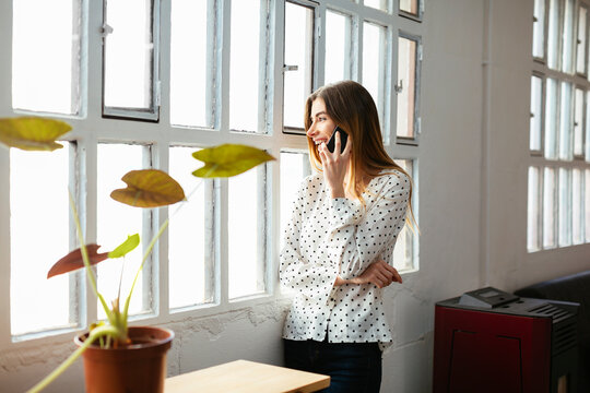 Happy young woman on cell phone at the window in office