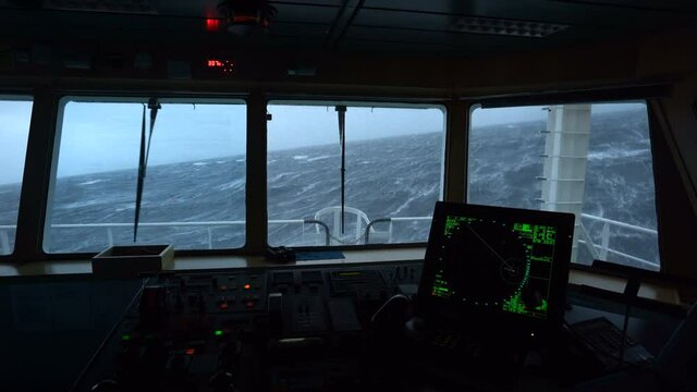 Ship in storm. View from bridge. View of radar and control panel. Strong pitching. High waves hit ship. White foam on water.