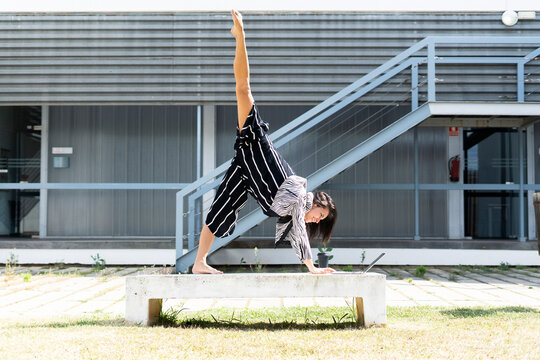 Female ballet dancer lifting her leg on a bench in front of an office building