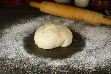 a mixture of yeast dough lies on a dark board sprinkled with white flour. a wooden rolling pin is located behind the dough. the process of making homemade pies and pizza. bread sourdough.
