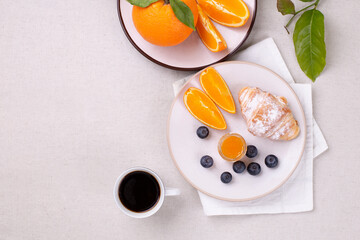 Breakfast with a cup of coffee, fresh croissant, jam and ripe blueberries and juicy oranges, on a white table, flat lay, copy space