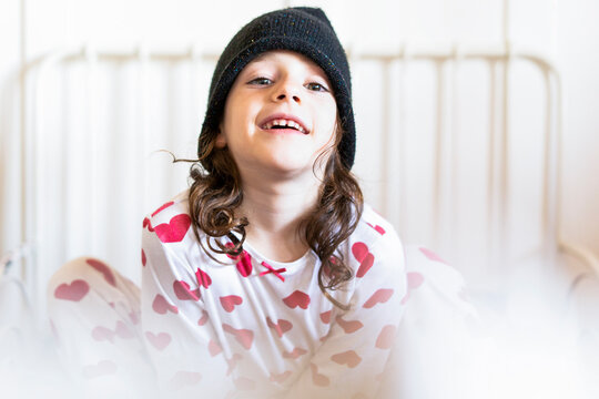 Portrait of smiling little girl sitting in bed wearing cap and pyjama
