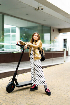Portrait of smiling girl with E-Scooter wearing golden sequin jacket and polka dot jumpsuit
