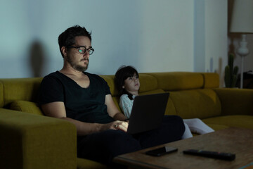 Father with daughter sitting on couch using laptop at night