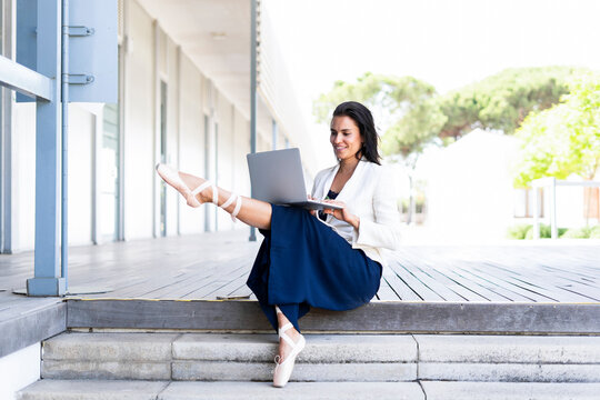 Female ballet dancer using laptop sitting on steps