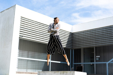 Female ballet dancer jumping on a bench in front of an office building