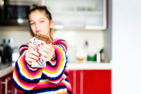 Girl in striped pullover in kitchen at home eating chocolate