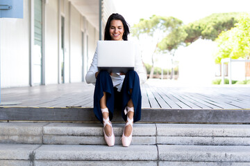 Female ballet dancer using laptop sitting on steps