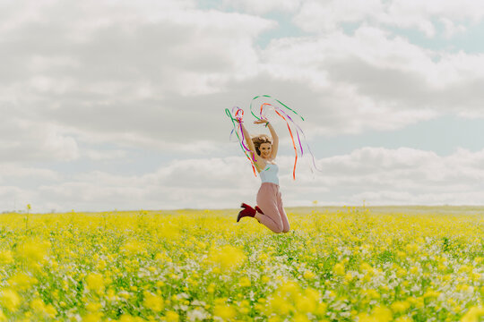 Happy young woman jumping with colourful ribbons in a flower meadow in spring