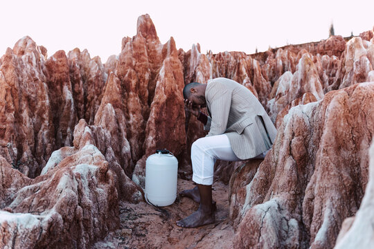 Desperate young man with empty water can sitting in rocky landscape