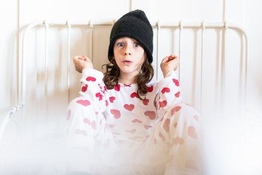 Portrait of starring little girl sitting in bed wearing cap and pyjama