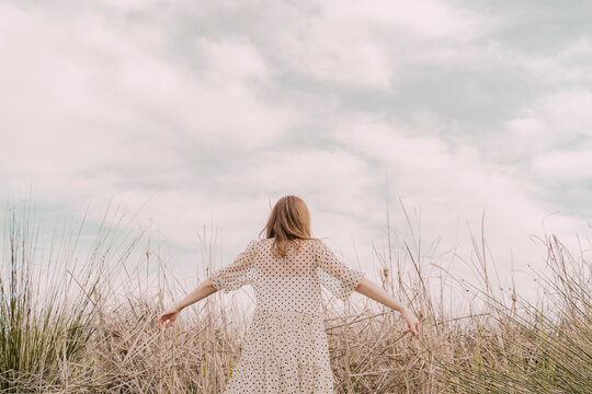Rear view of woman in vintage dress with outstretched arms at a remote field in the countryside