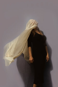 Woman under cloth in front of gray wall