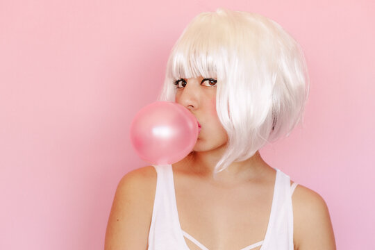 Portrait of young woman with pink gum bubble in front of pink background