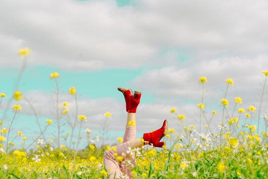 Legs of a woman wearing red ankle boots lying in a flower meadow in spring