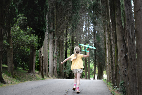 Girl with toy plane running on a treelined road