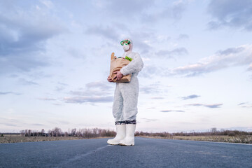 Man wearing protective suit and mask holding grocery bag on a country road