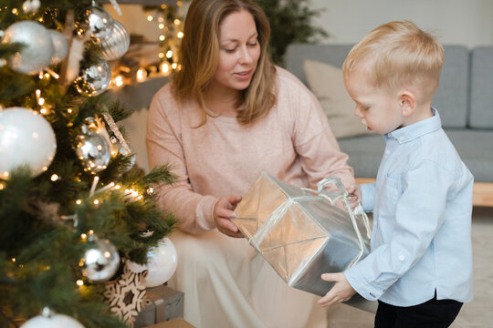 Mother giving present to her little son near Christmas tree