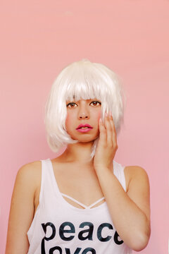 Portrait of young woman wearing white wig in front of pink background