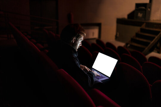Director sitting at auditorium of theatre working on laptop