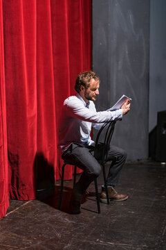 Rehearsing actor sitting on theatre stage looking at script