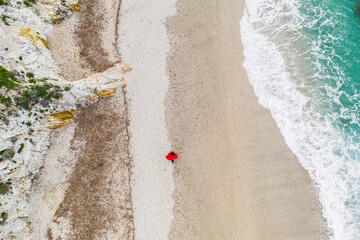 Italy, Elba, woman with red coat walking at beach, aerial view with drone