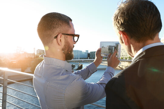Two businessmen taking a picture with tablet on a bridge in the city