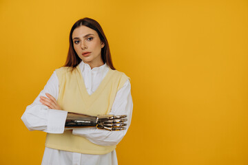 Confident young woman in shirt and vest with new bionic prosthesis crosses arms standing on yellow...