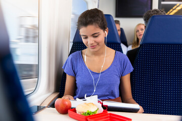 Teenage girl traveling alone by train, listening music, eating a snack