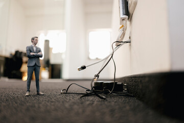 Businessman figurine standing in office, looking at disconnected cables