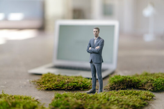 Businessman figurine with laptop standing on green moss