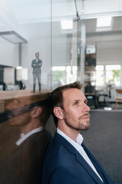 Businessman sitting in his office with his 3D portrait behind a glass pane