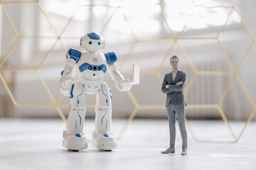 Miniature businessman figurine standing next to robot with laptop