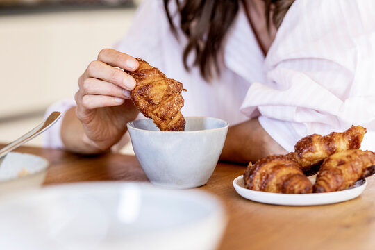 Close-up of woman dipping a croissant into coffee cup