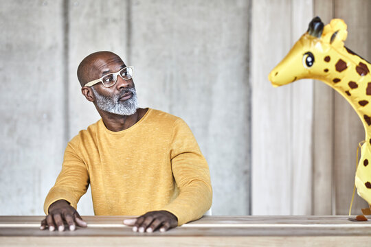 Surprised mature businessman sitting at desk in office looking at giraffe figurine