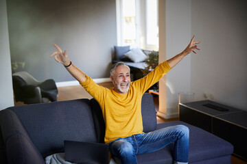 Mature man sitting on couch at home cheering