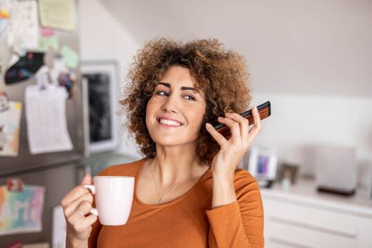 Woman holding cell phone and coffee cup at home