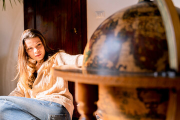 Young woman sitting by globe, looking for travel destinations