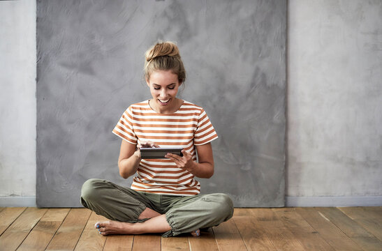 Smiling young woman sitting on the floor using a digital tablet