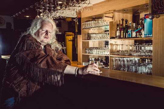 Portrait of blond rocker wearing brown leather jacket standing at counter of an old-fashioned pub