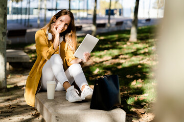 Smiling woman sitting on a bench in a park using tablet