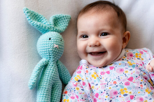 Baby girl with a stuffed bunny toy lying on bed
