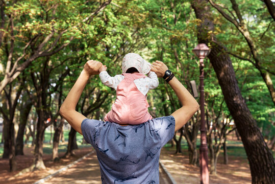 Father walking in a park with baby girl on his shoulders